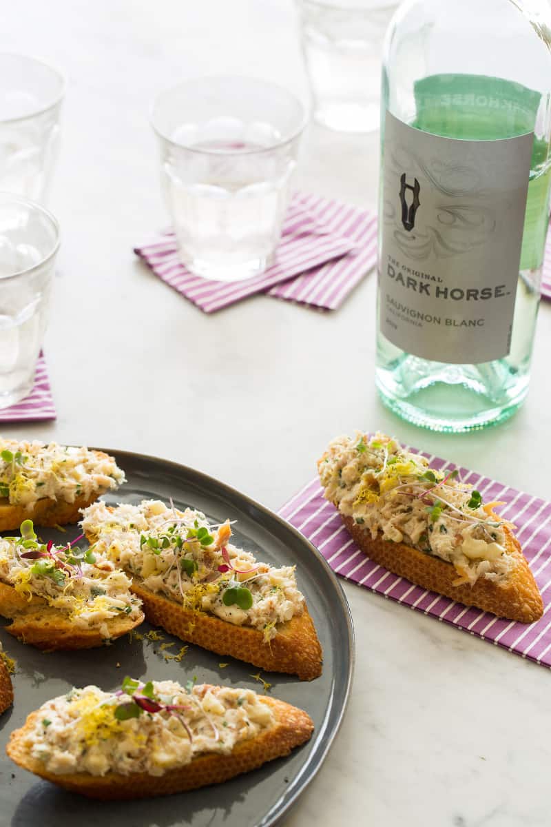 A plate of smoked trout on toast with a wine bottle and glasses with napkins.