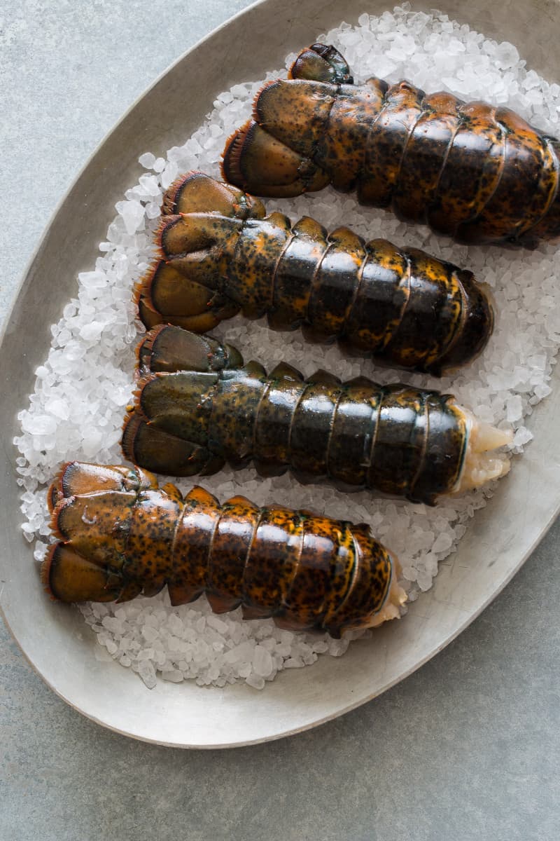 A plate of uncooked lobster tails in the shells.