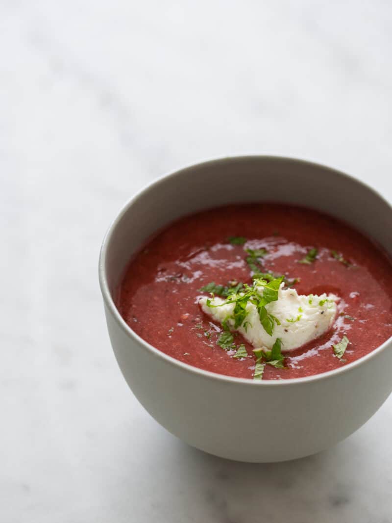 A single bowl of strawberry and tomato gazpacho on a marble surface.  