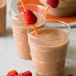 A close up of peach, papaya, and raspberry smoothies garnished with skewered raspberries.