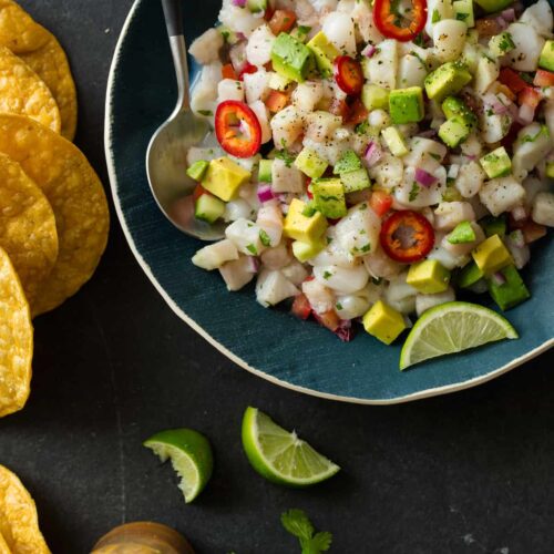 A bowl of simple ceviche with a spoon, chips and lime wedges.