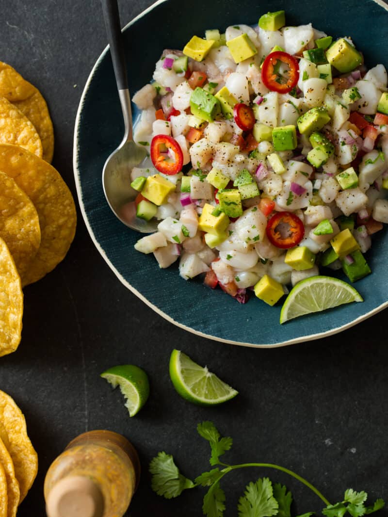 Simple ceviche in a blue bowl with a spoon, lime wedges, and tostadas.