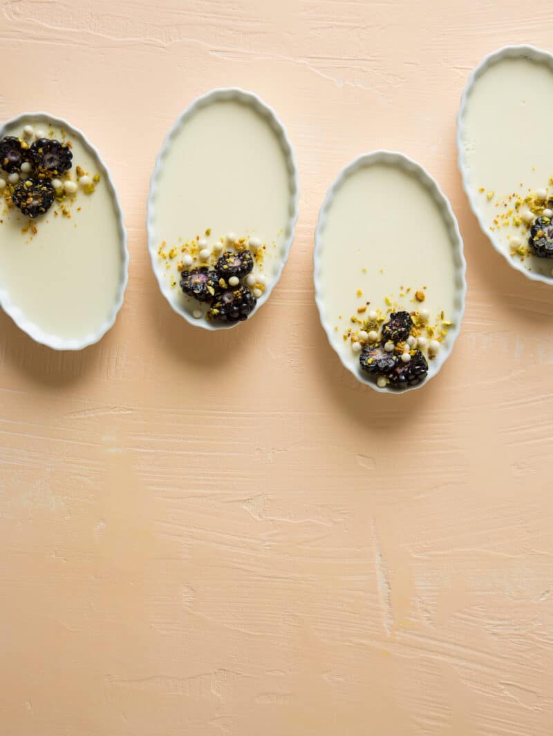 Several creme fraiche panna cotta garnished with blackberries, pistachios, and white chocolate crispy balls.