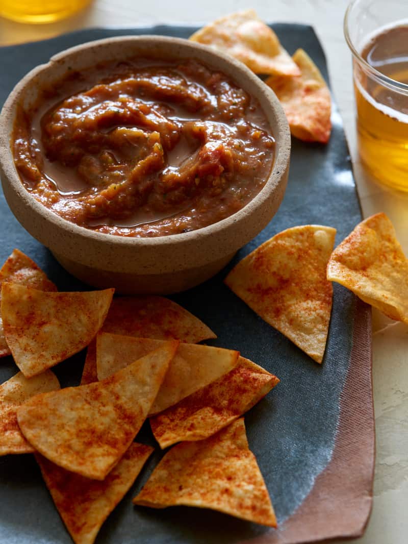 A bowl of roasted tomato salsa on a plate of tortilla chips and beer.