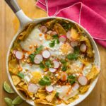 Green chilaquiles in a pan on a wooden surface with a pink linen.