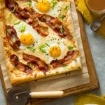 A breakfast tart on parchment paper and a wooden cutting board with a pizza cutter.