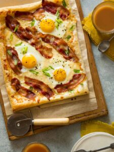 A breakfast tart on parchment paper and a wooden cutting board with a pizza cutter.