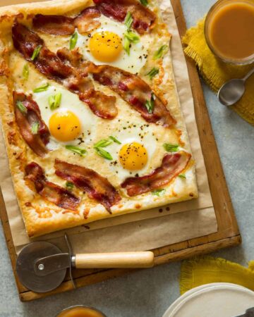 A breakfast tart on parchment paper and a wooden cutting board with a pizza cutter.
