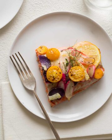 A piece of stacked salmon on a white plate with a fork.