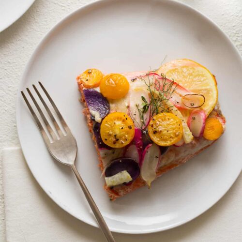 A piece of stacked salmon on a white plate with a fork.