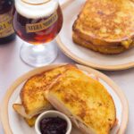 Monte cristo sandwiches with a ramekin of cranberry jam on plates with beer.