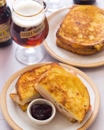 Monte cristo sandwiches with a ramekin of cranberry jam on plates with beer.