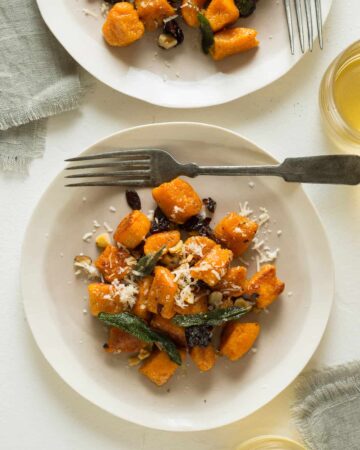 Plates of sweet potato gnocchi with fried sage dried cherries and toasted hazelnuts with a fork.