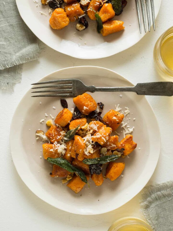 Plates of sweet potato gnocchi with fried sage dried cherries and toasted hazelnuts with a fork.