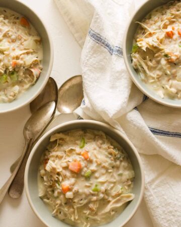 Creamy chicken and faro soup in bowls with linens and spoons.
