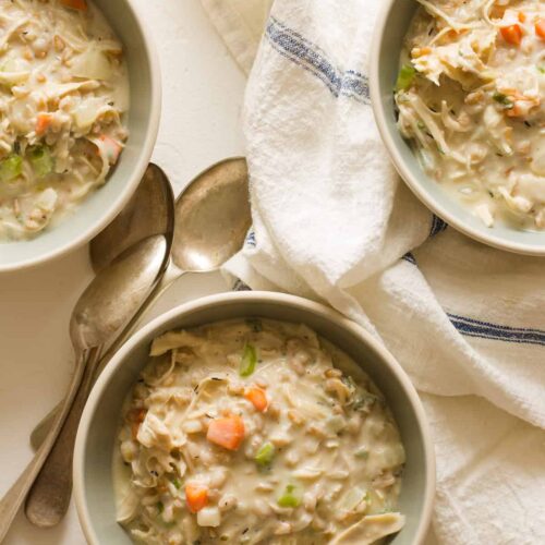 Creamy chicken and faro soup in bowls with linens and spoons.