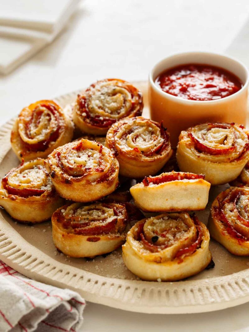 A platter of pizza wheels with a bowl of marinara dipping sauce. 