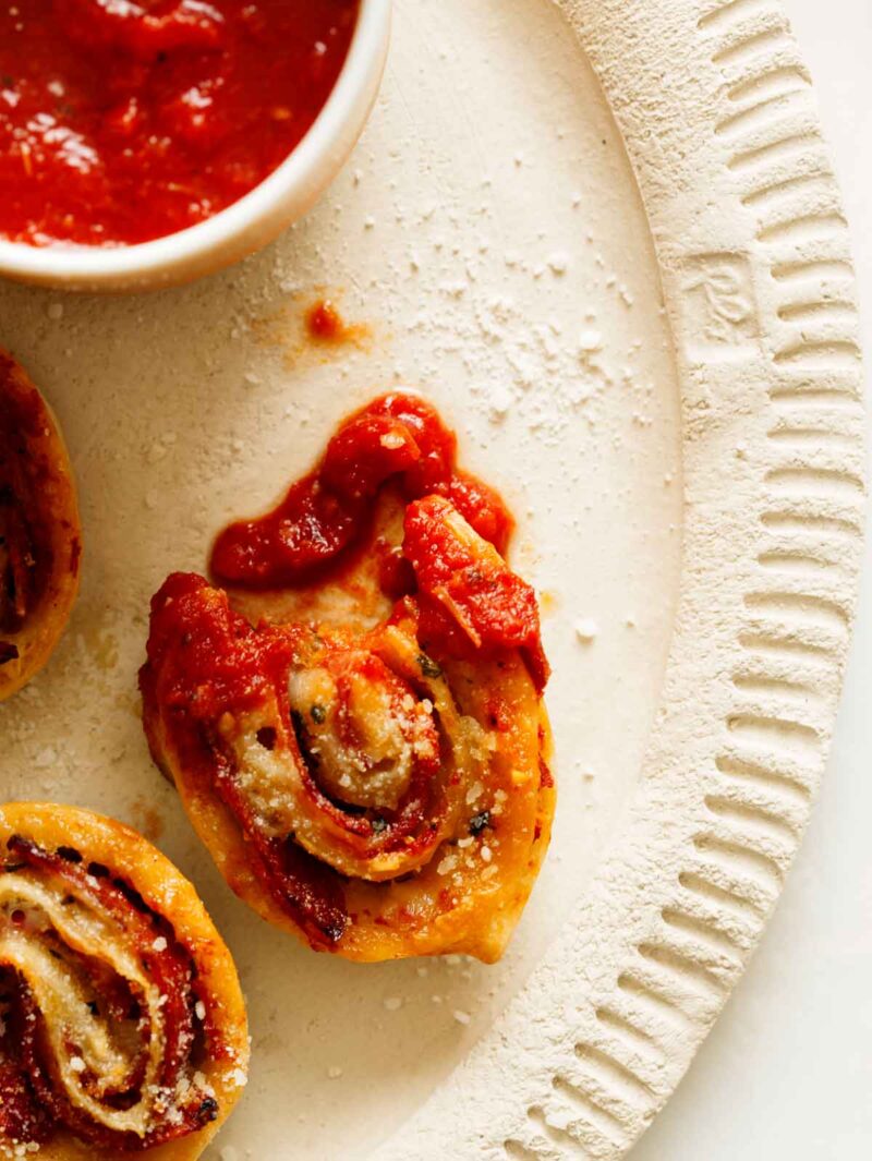 A pizza pin wheel dipped in marinara sauce with a bite taken out of it. 