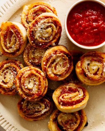 A close up of pizza wheels with a ramekin of marinara sauce on a plate.