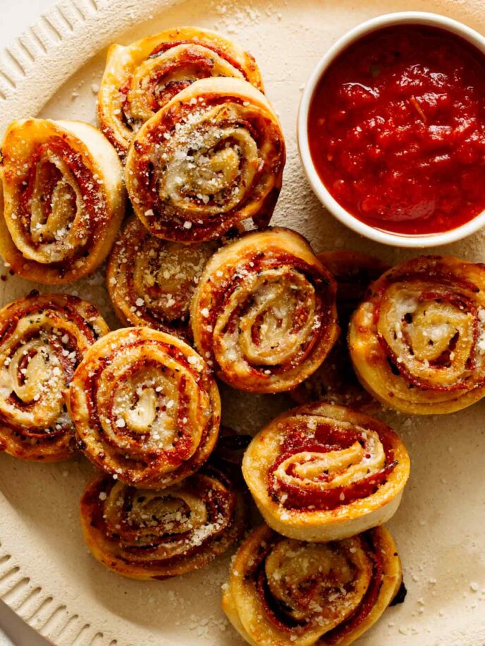 A close up of pizza wheels with a ramekin of marinara sauce on a plate.