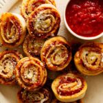 A close up of pizza wheels with a ramekin of marinara sauce on a plate.