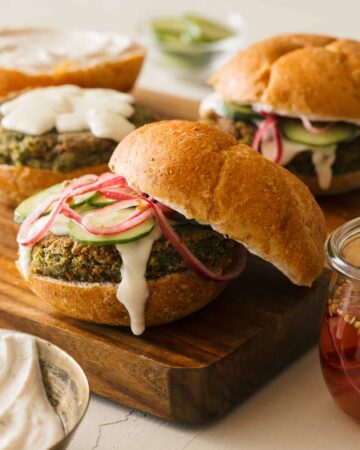 Falafel burgers with veggies and sauce on a wooden cutting board.