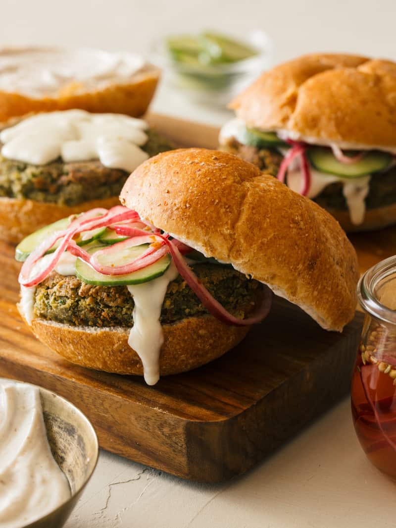 A close up of falafel burgers with roasted garlic aioli, quick pickled red onions, and cucumbers.