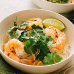 A bowl of yum wood sen with shrimp garnished with cilantro and a lime wedge.