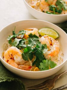 A bowl of yum wood sen with shrimp garnished with cilantro and a lime wedge.