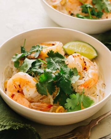 A bowl of yum wood sen with shrimp garnished with cilantro and a lime wedge.