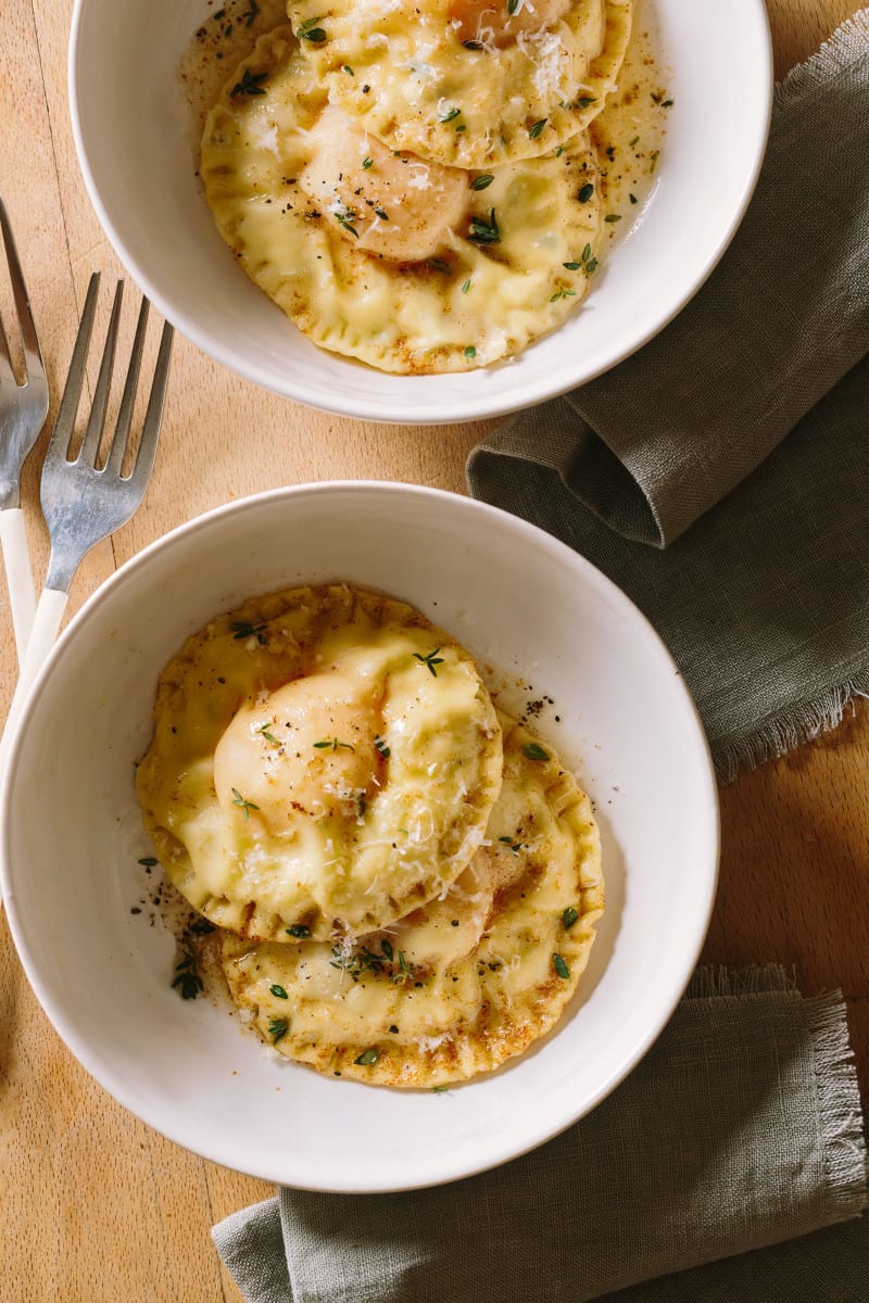 Bowls of chicken and tarragon poached yolk stuffed ravioli with forks.