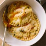 Chicken and tarragon poached yolk stuffed ravioli in a bowl with a fork.