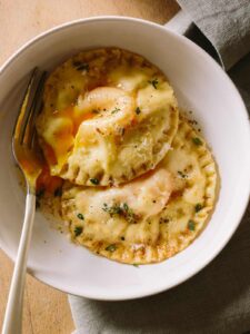Chicken and tarragon poached yolk stuffed ravioli in a bowl with a fork.