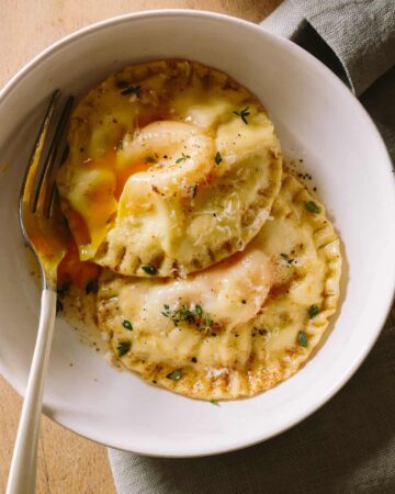 Chicken and tarragon poached yolk stuffed ravioli in a bowl with a fork.