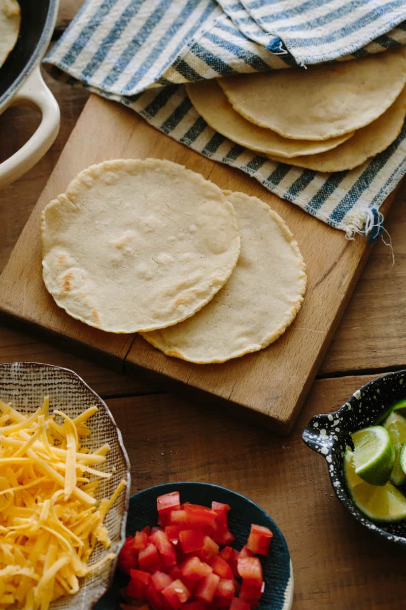 Homemade corn tortillas on a cutting board with toppings next to it. 