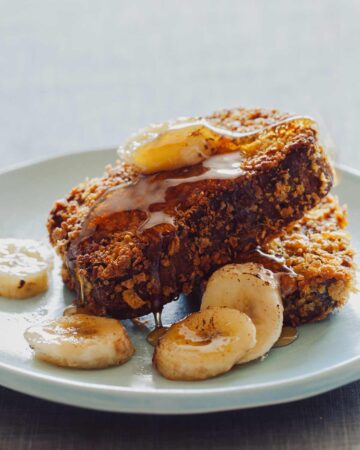 Two pieces of banana bread french toast with caramelized bananas and maple syrup on a plate.