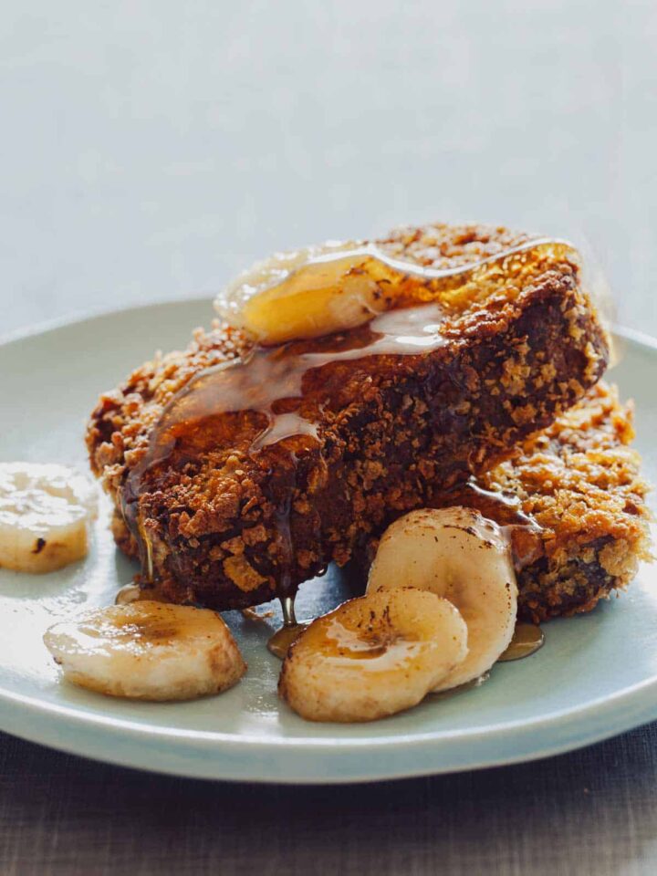 Two pieces of banana bread french toast with caramelized bananas and maple syrup on a plate.