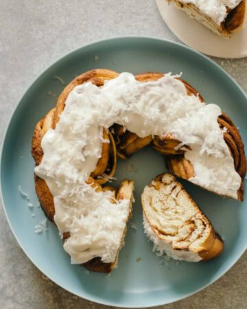 Brown butter braided cinnamon roll cake topped with shredded coconut on a plate.