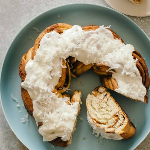 Brown butter braided cinnamon roll cake topped with shredded coconut on a plate.