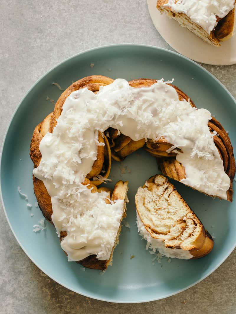 A sliced brown butter braided cinnamon roll cake topped with icing and shredded coconut.