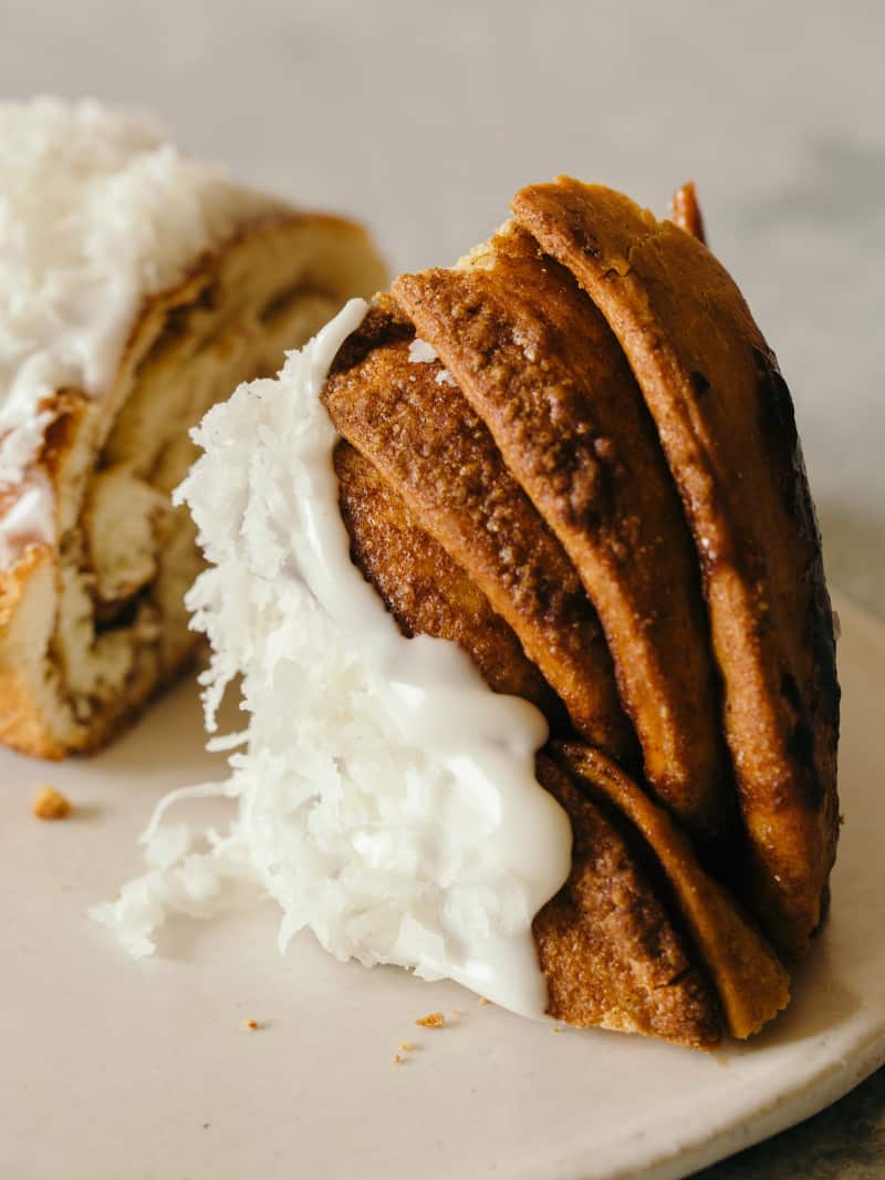 A close up of a slice brown butter braided cinnamon roll cake topped with shredded coconut.