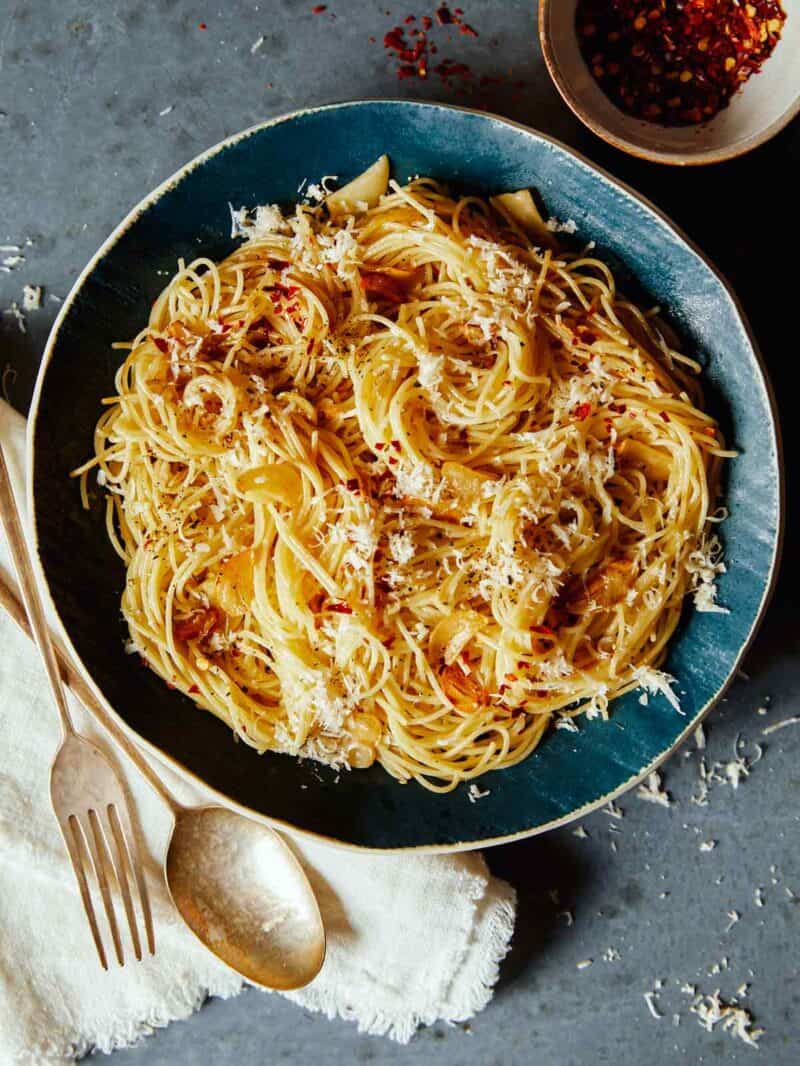 Capellini with garlic lemon and parmesan on a blue plate with a fork and spoon.