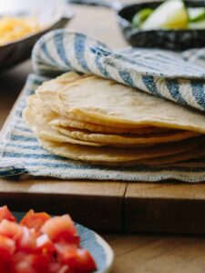 Homemade corn tortillas a hand towel on a wooden cutting board.