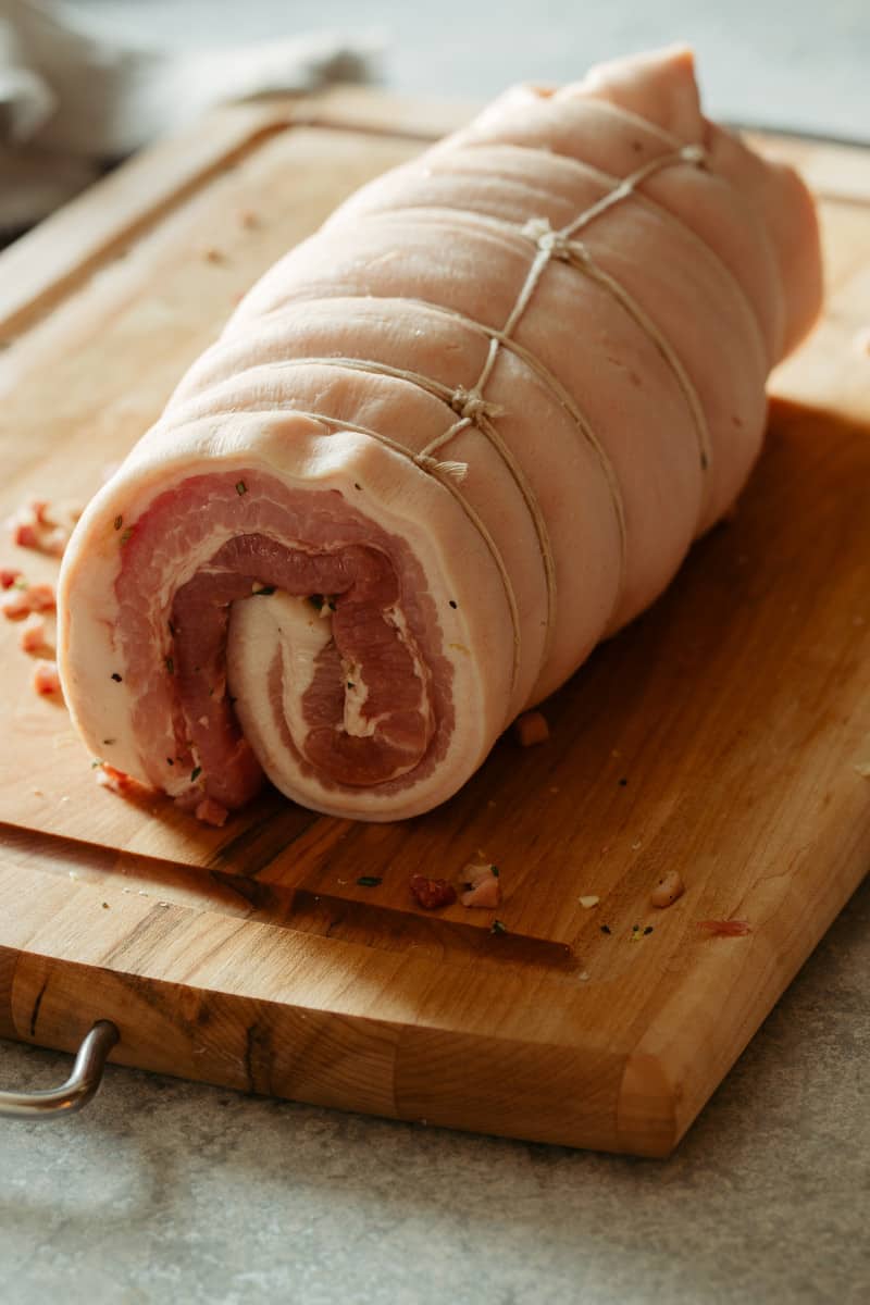 A close up of raw pork belly rolled up on a cutting board.