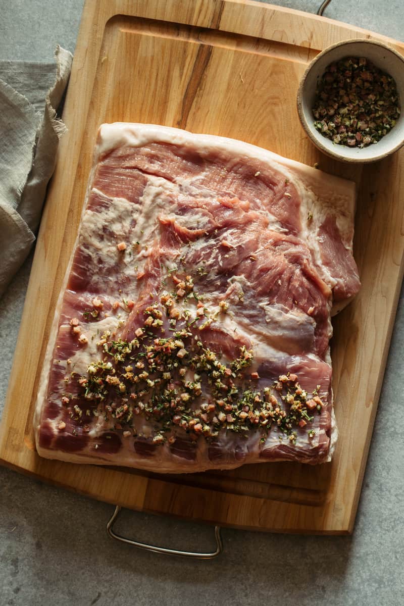 Raw pork belly with spices on a cutting board.