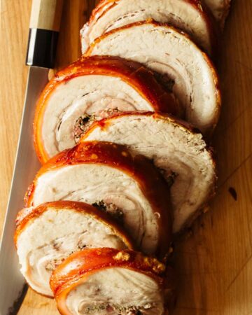 A close up of sliced pork belly porchetta with a knife.