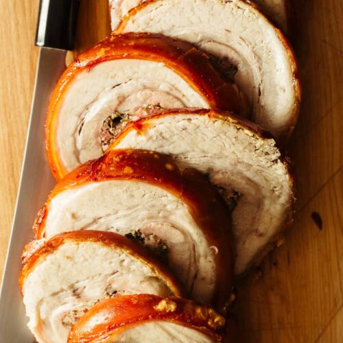 A close up of sliced pork belly porchetta with a knife.