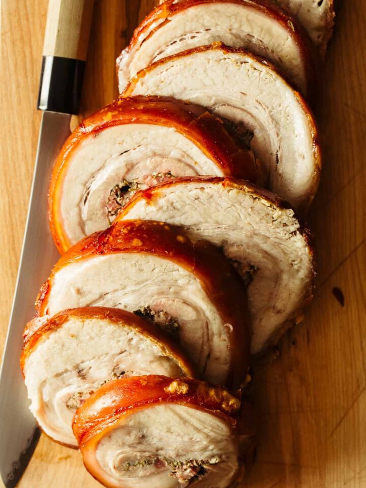 A close up of sliced pork belly porchetta with a knife.