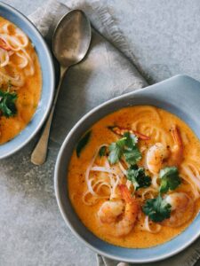 Bowls of spicy red curry and coconut noodle soup with shrimp with a spoon.