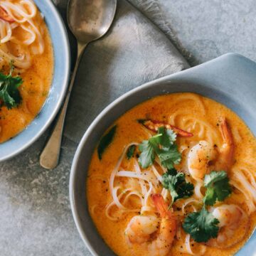 Bowls of spicy red curry and coconut noodle soup with shrimp with a spoon.